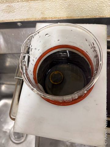 The ring is in a dark liquid at the bottom of a beaker